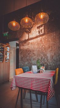 A cozy restaurant interior featuring rustic lighting, colorful chairs, and a red checkered tablecloth.