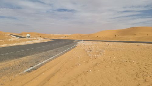 Free A solitary road winds through an expansive and serene desert landscape under a cloudy sky. Stock Photo
