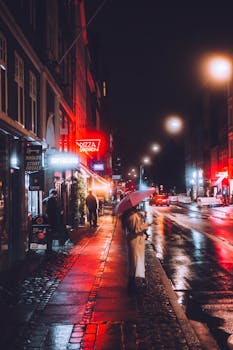 Atmospheric night scene of a Copenhagen street with neon lights and reflections on wet pavement.
