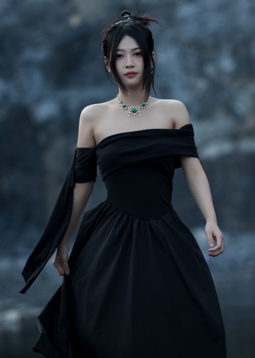 Free Woman in an off-shoulder black dress with necklace in an outdoor setting. Stock Photo