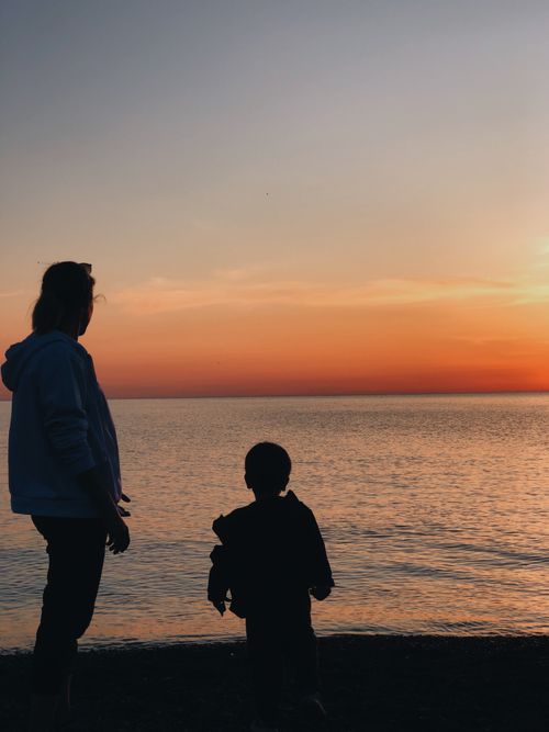 Free A serene sunset silhouette of an adult and child by the beach, creating a peaceful scene. Stock Photo