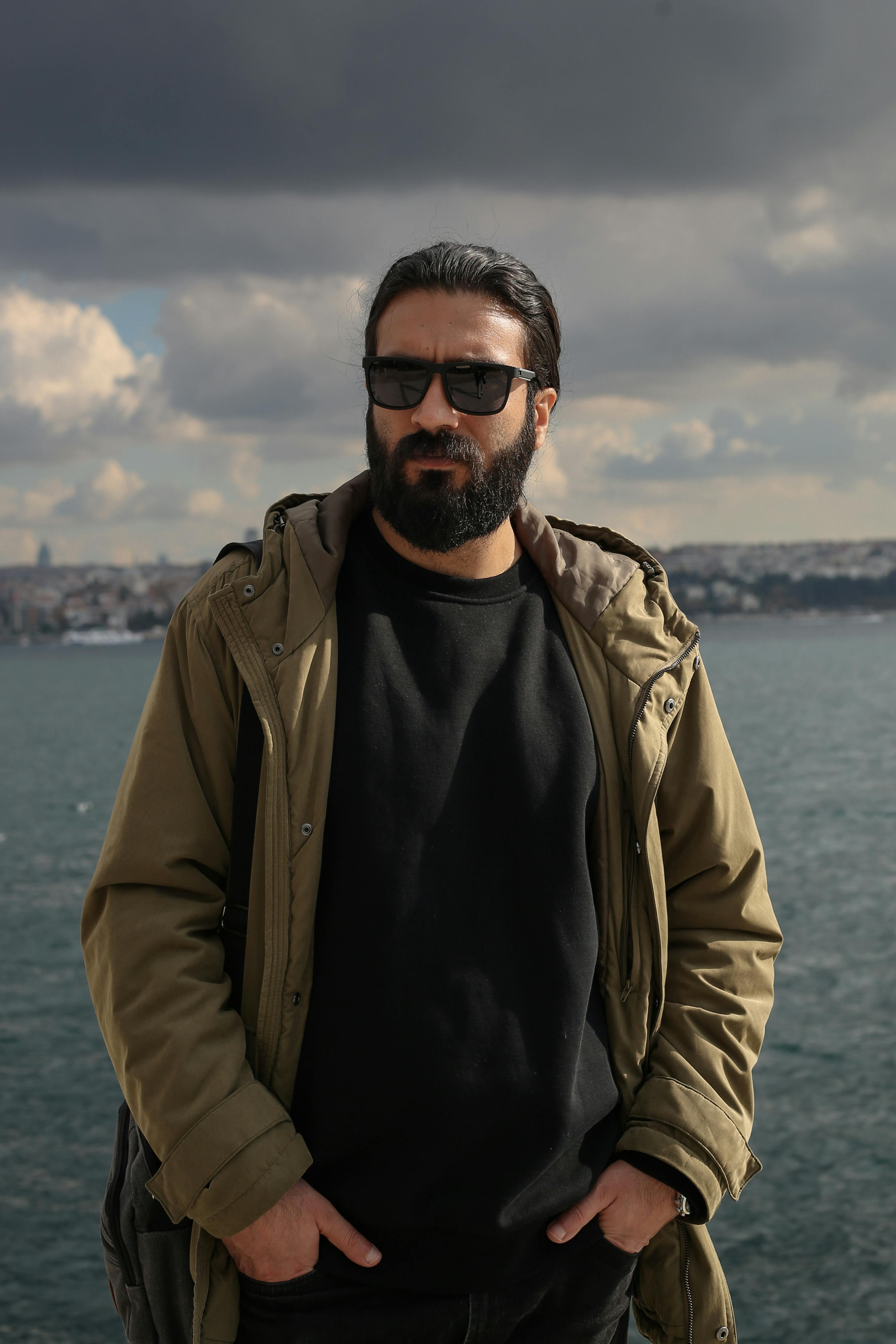 Bearded man in Istanbul with a scenic waterfront backdrop and moody sky.