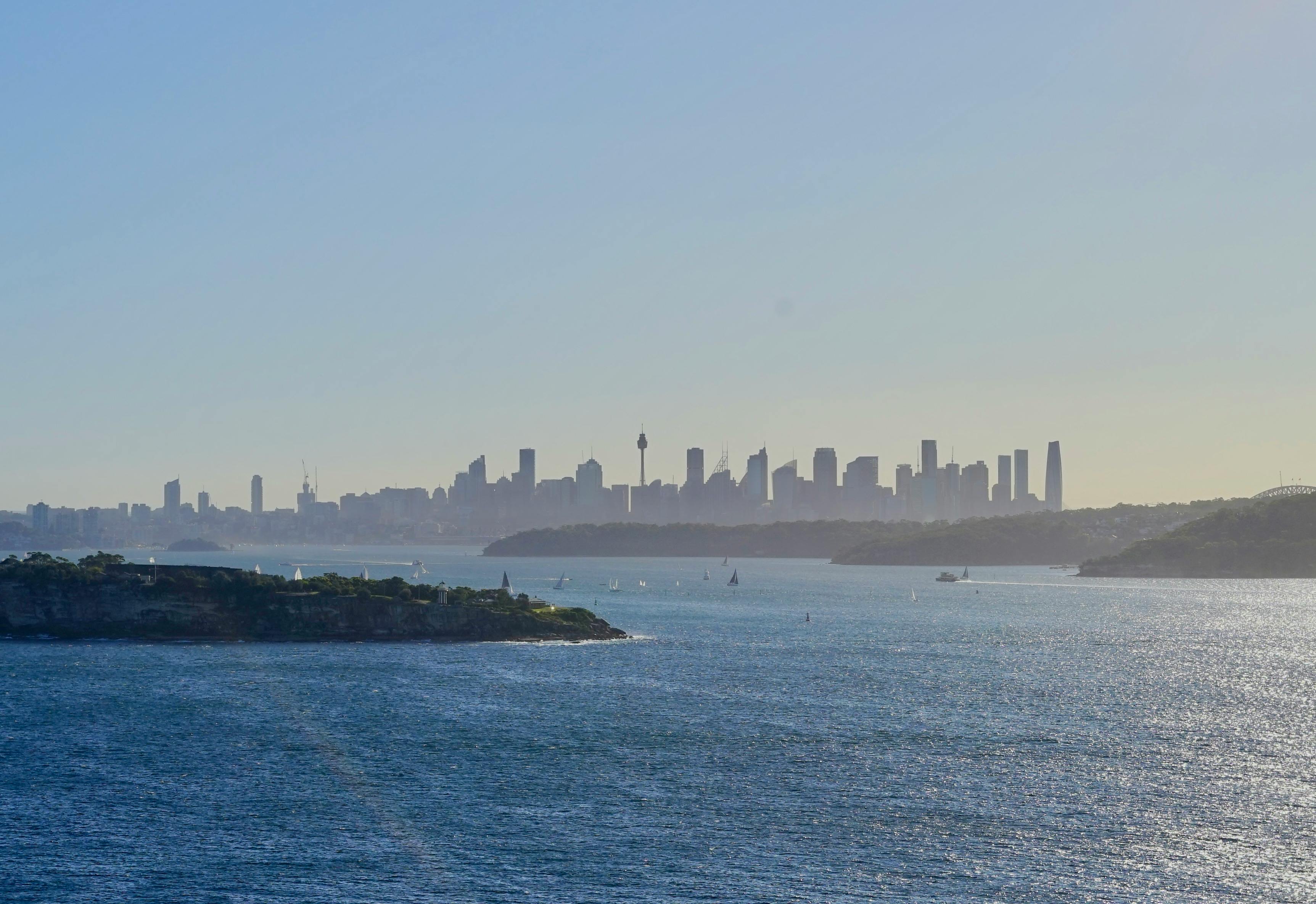 Aerial view of Sydney harbor with the skyline in the background under a clear blue sky.