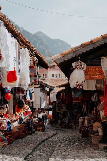 Quaint European market street lined with traditional costumes and textiles under a bright sky.