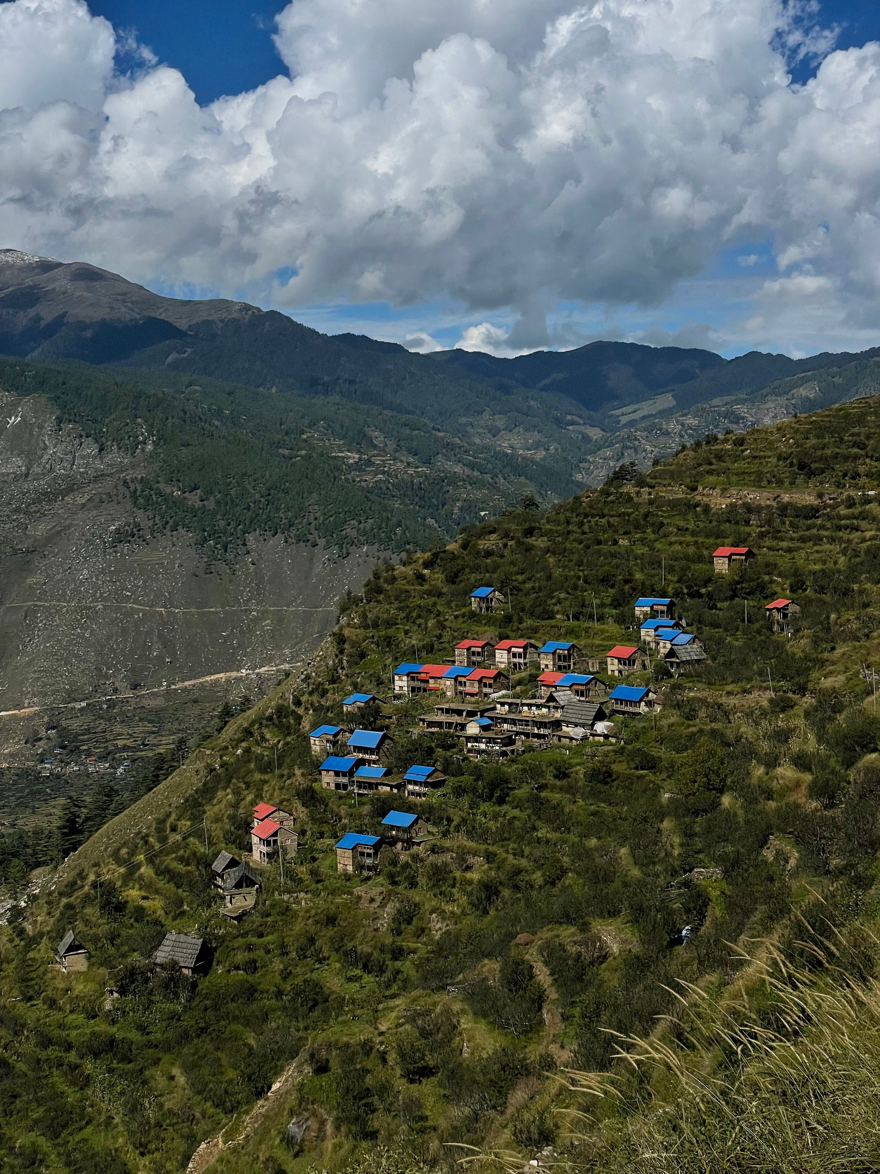 Colorful village nestled in mountain landscape with blue roofs under a cloudy sky.