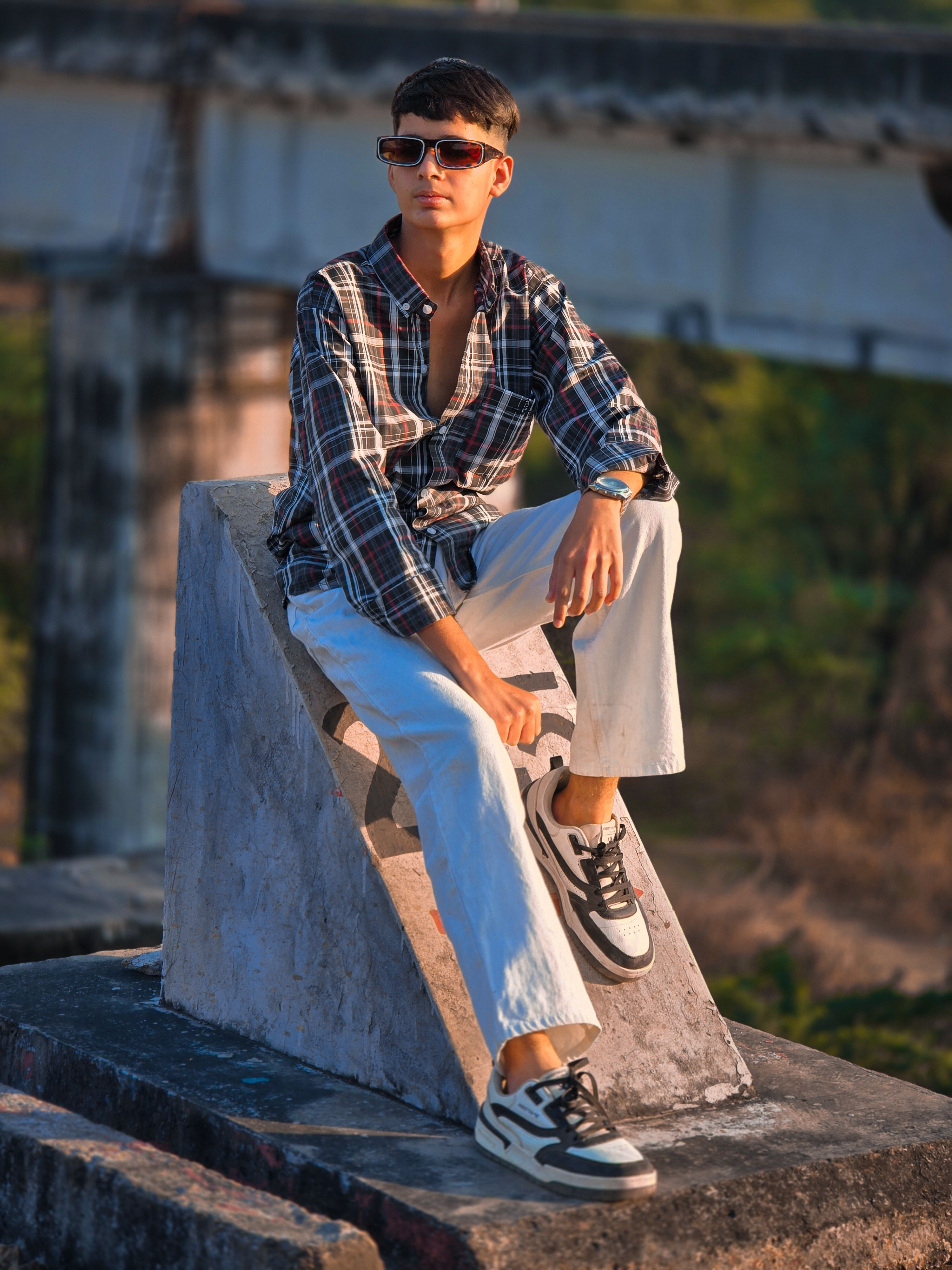 Stylish young man in sunglasses poses outdoors in casual attire on a sunny day.