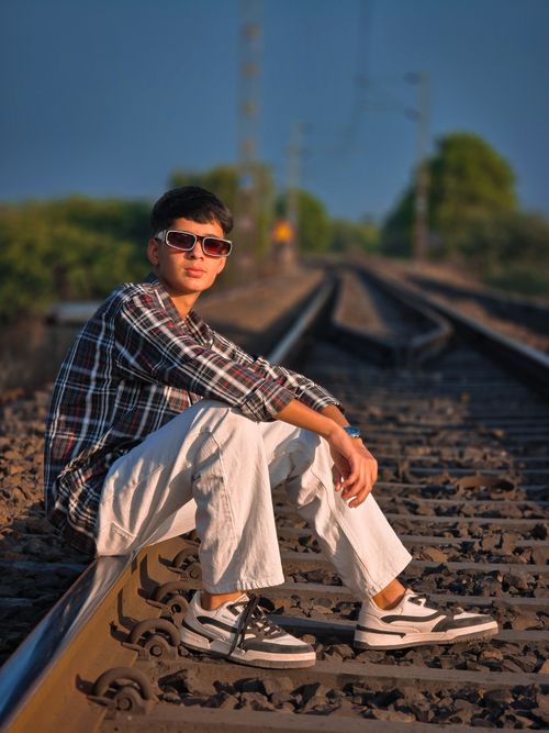 Free A relaxed young man wearing sunglasses and fashionable clothes sits confidently on railroad tracks outdoors. Stock Photo