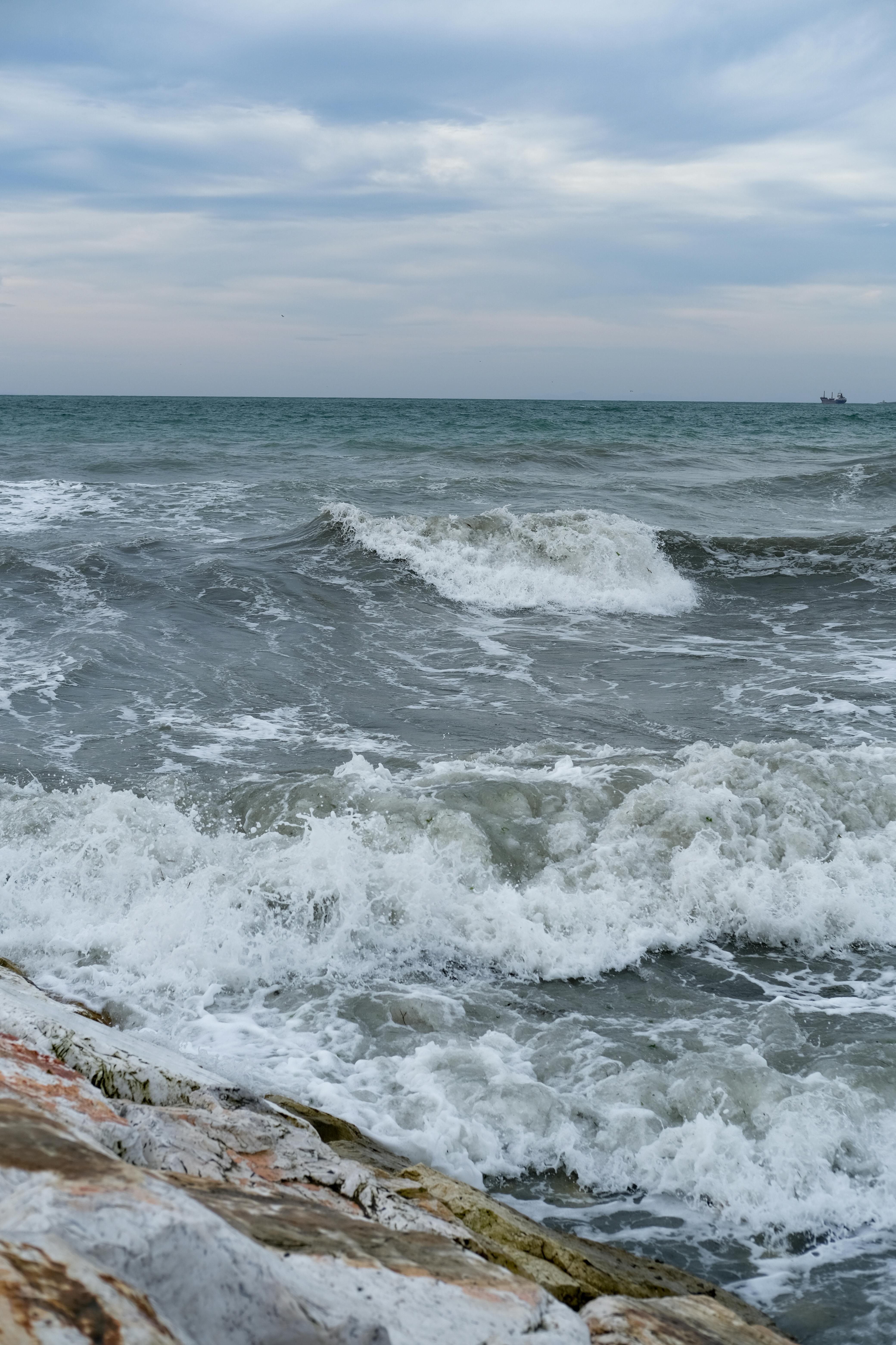 A striking view of powerful waves crashing on Büyükçekmece's rocky shore under a cloudy sky.