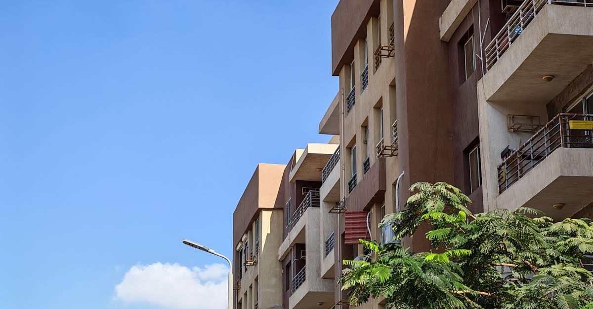 Urban apartment building against a bright blue sky with foliage in the foreground.
