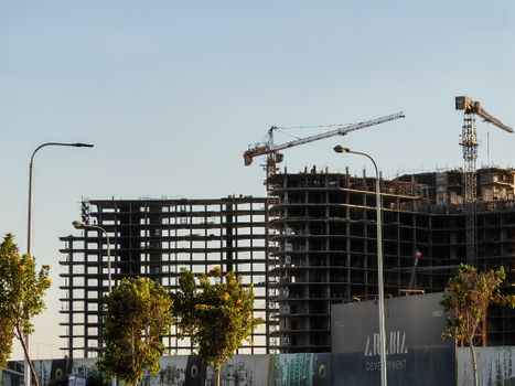 High-rise building under construction with cranes and trees in the forefront.