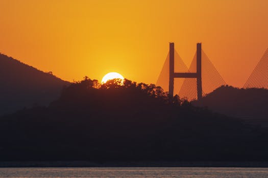 A stunning sunset over a bridge and hills creating a dramatic silhouette scene.