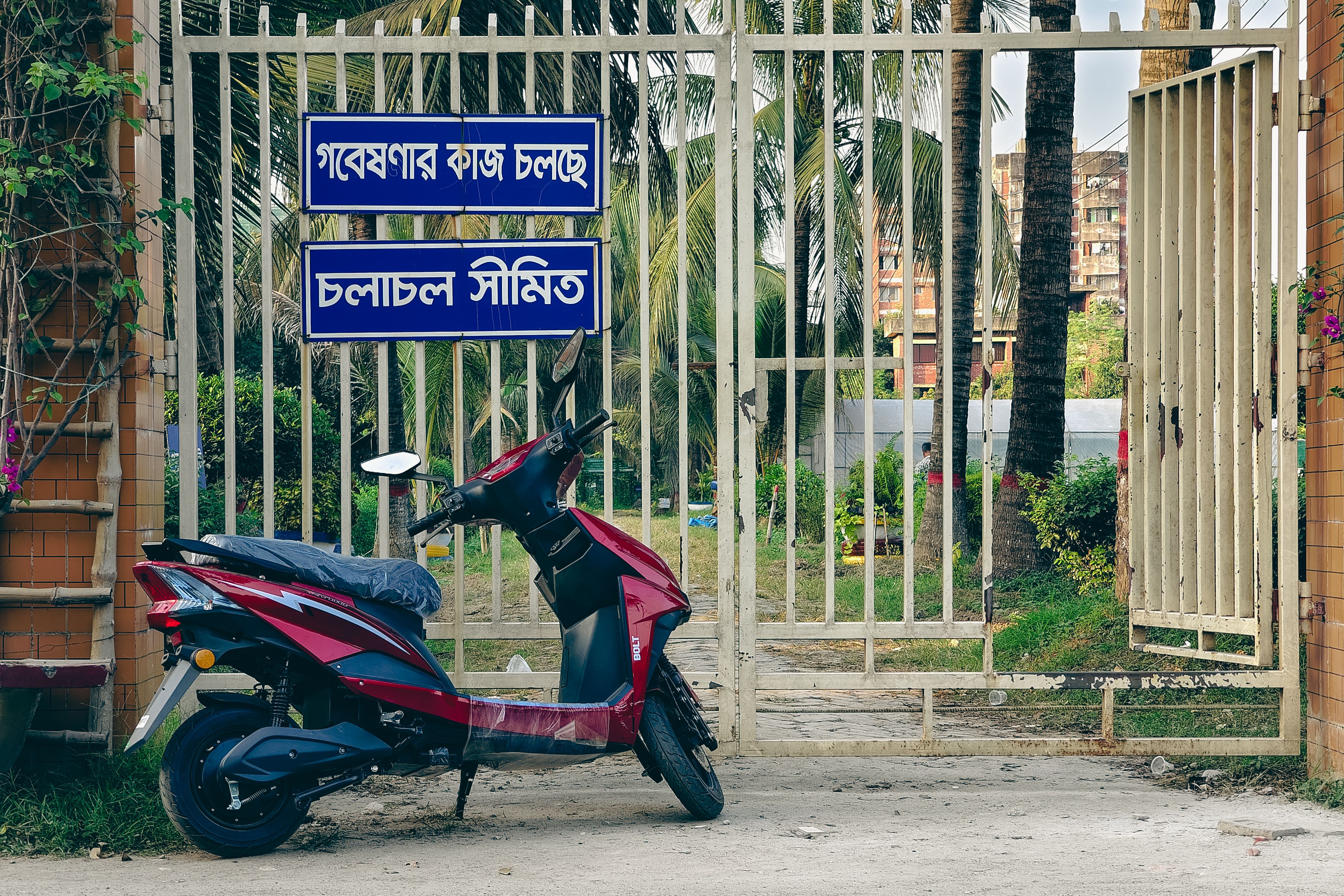 An electric scooter parked near a gated entrance with palm trees in the background, suggesting tranquility and urban lifestyle.