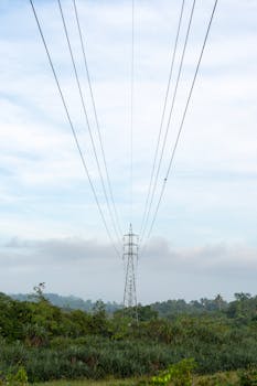 A tall electricity pylon with power lines in a green field against a cloudy sky.