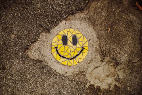 Free Colorful mosaic smiley face embedded in cracked urban pavement, showcasing unique street art. Stock Photo