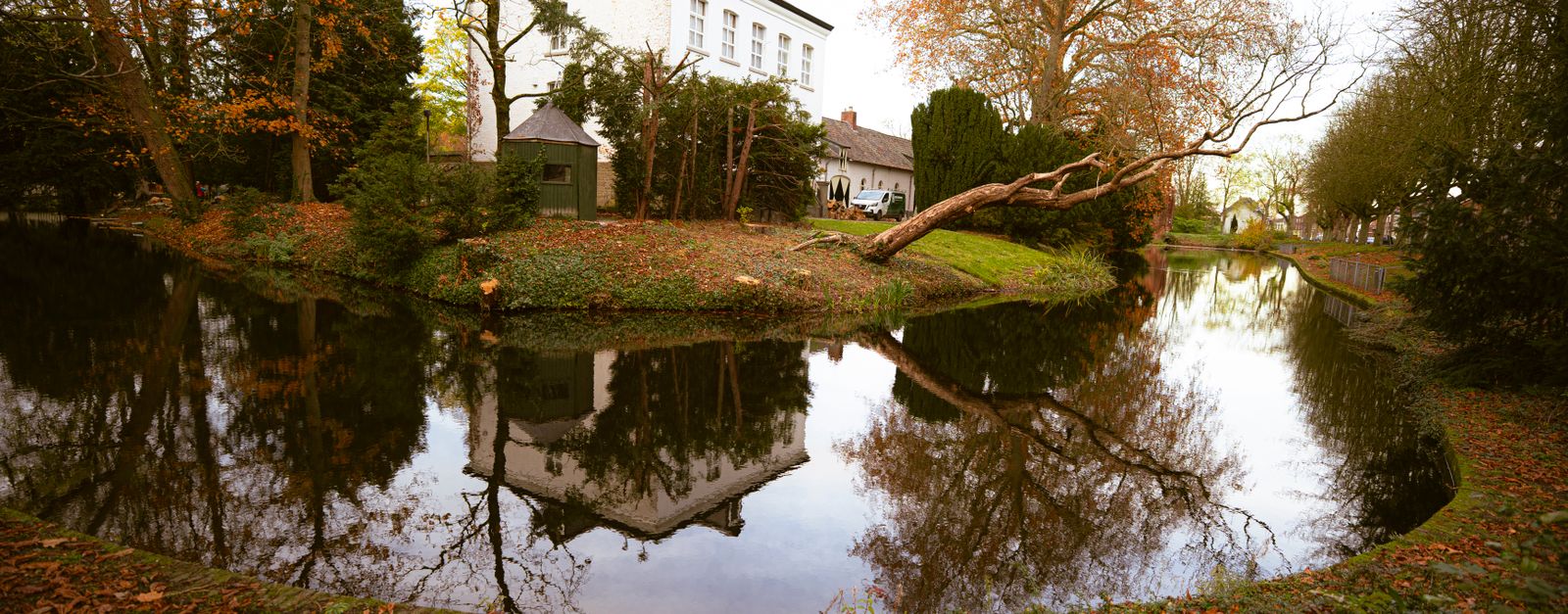 A beautiful reflection of a historic building on a tranquil canal surrounded by autumn trees in Weert, Limburg.