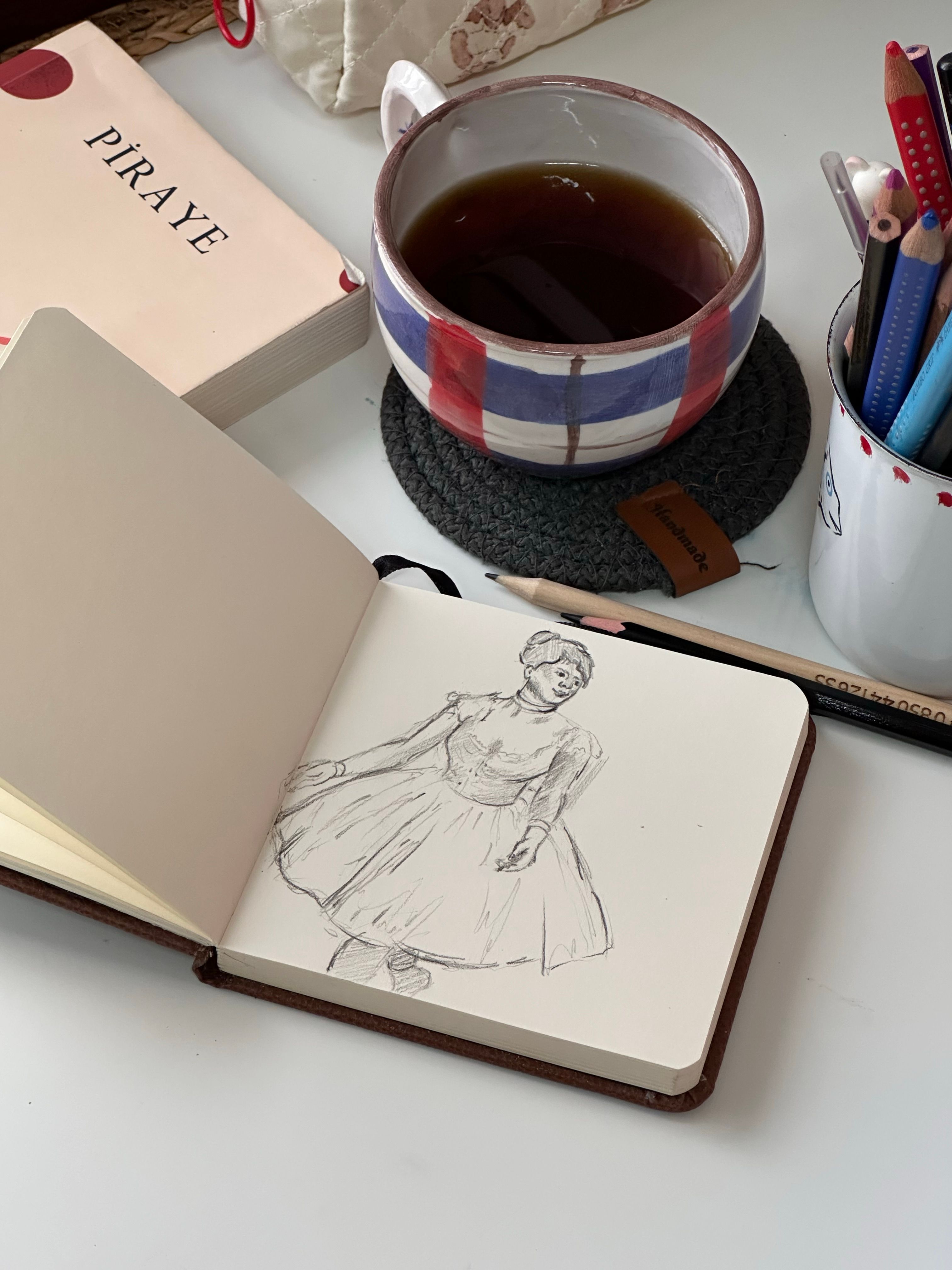 A creative desk setup featuring a sketchbook, tea, and stationery, ideal for artists.
