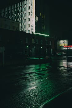 Moody nighttime street scene with reflections and urban architecture.