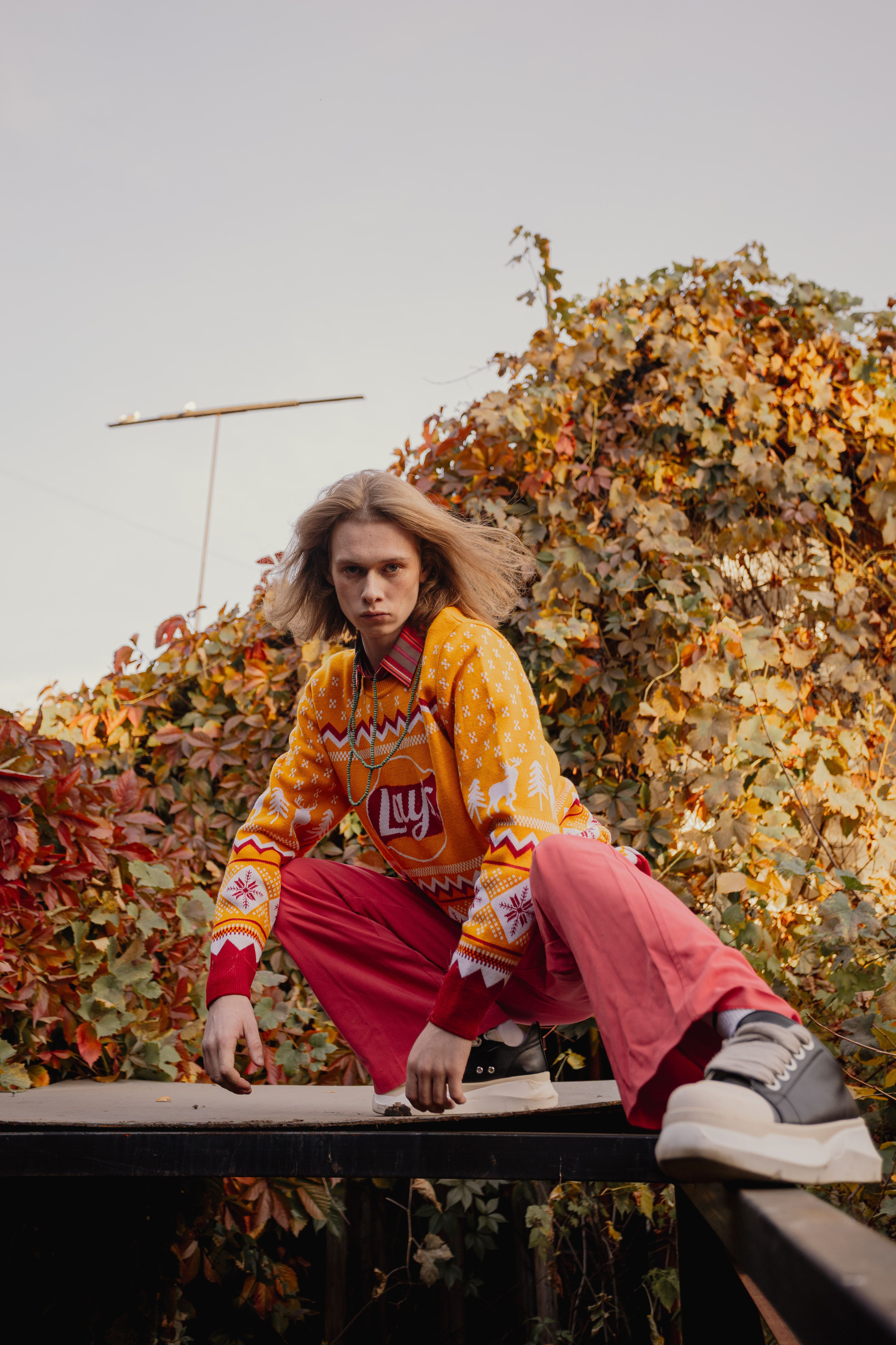 A stylish young man poses in an autumn landscape wearing colorful clothing.