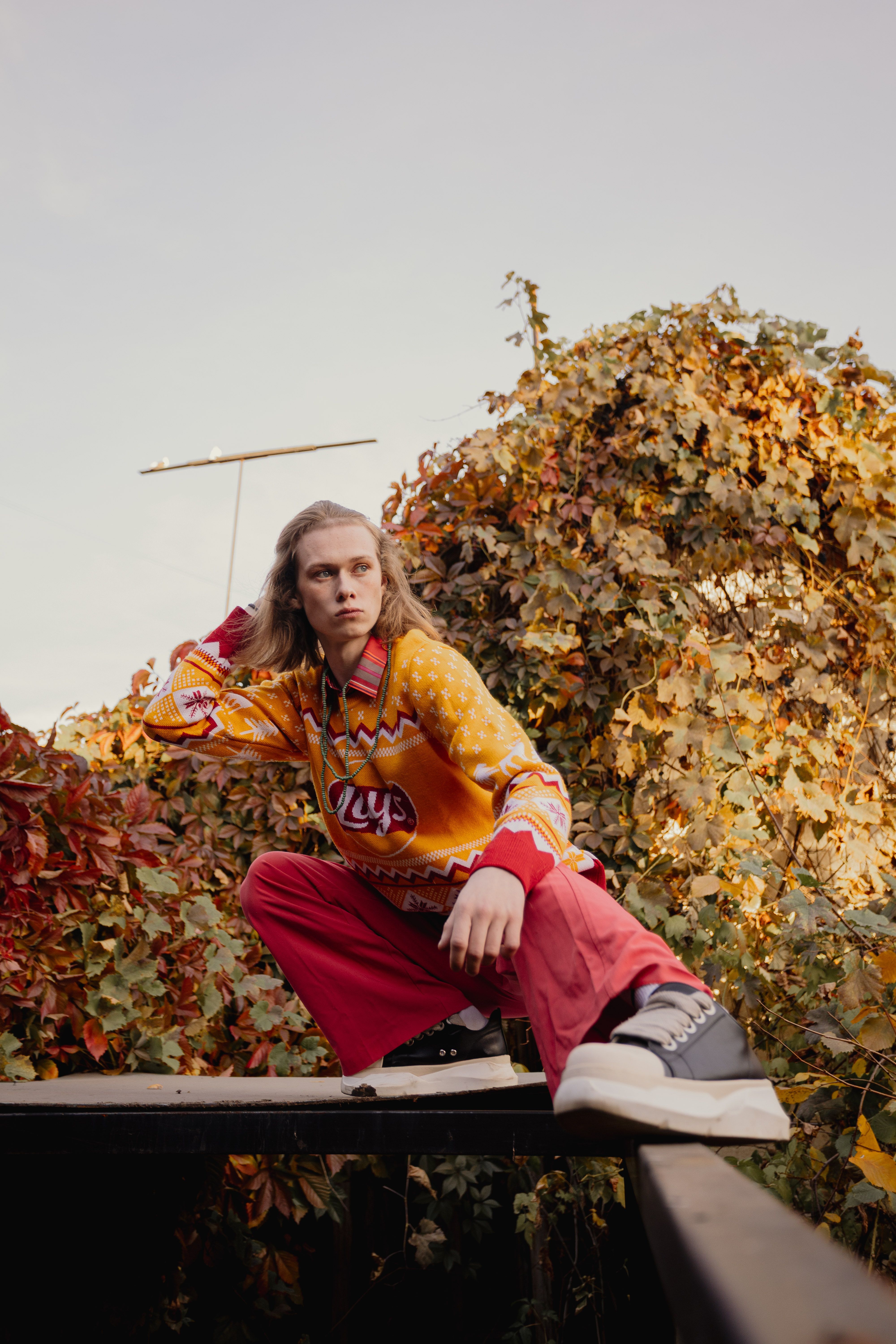 Young adult in vibrant outfit posing outdoors surrounded by fall foliage.