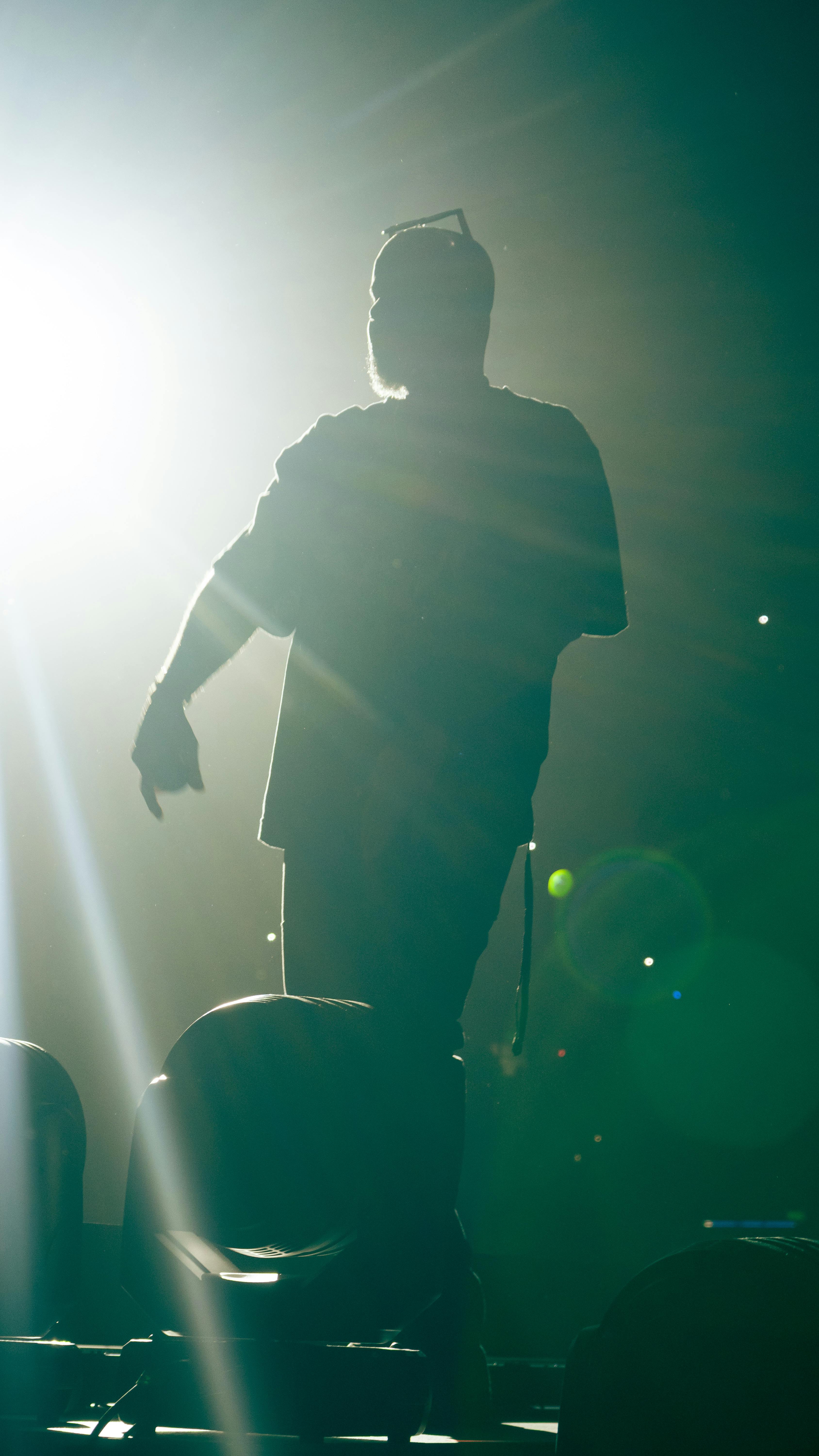 Free Dramatic silhouette of a performer on stage illuminated by a bright spotlight, creating a vibrant concert scene. Stock Photo