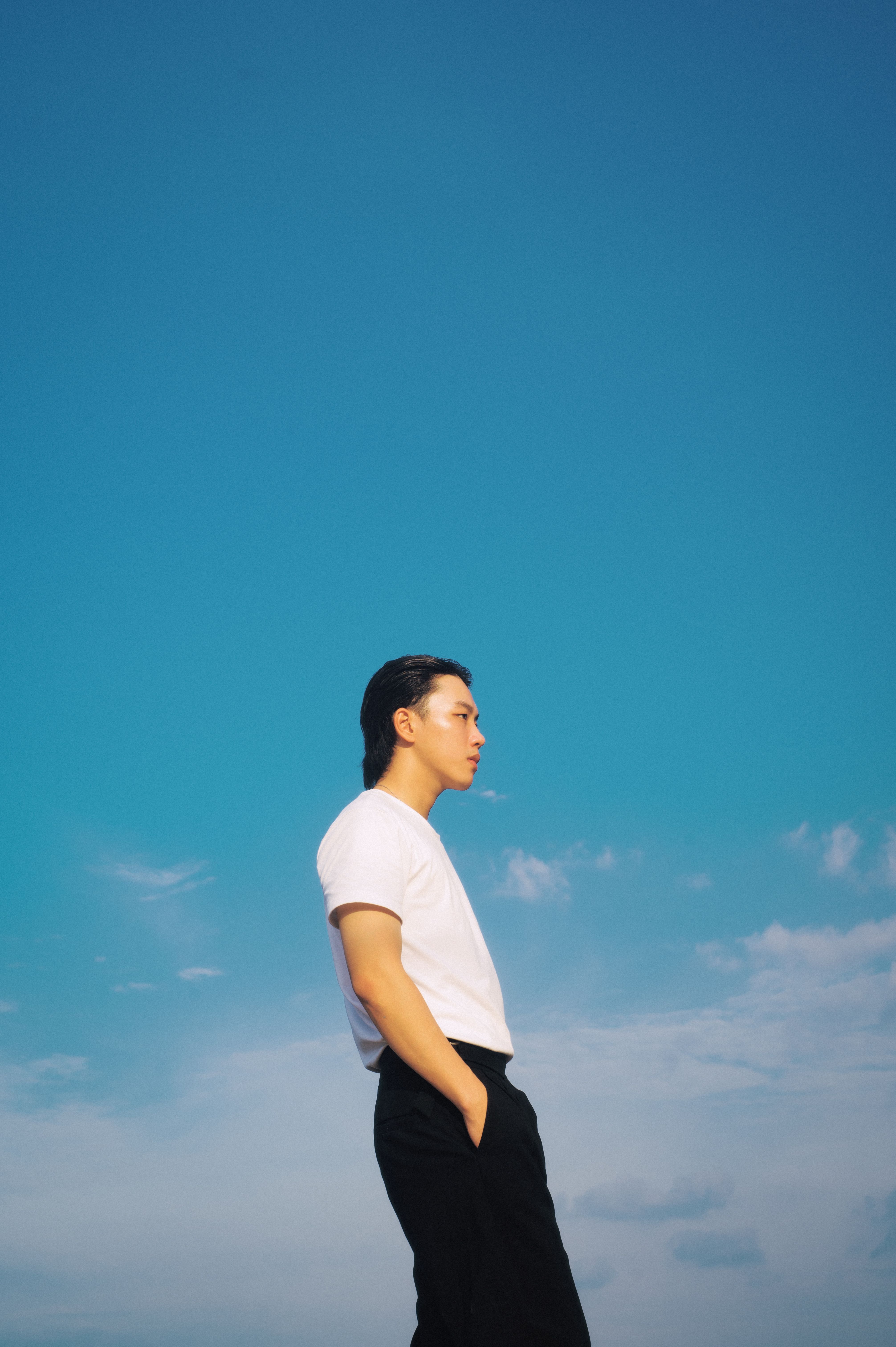 Profile view of young adult under vibrant sky, hands in pockets.