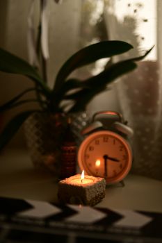 Warm cozy scene with lit candle and vintage alarm clock on table.