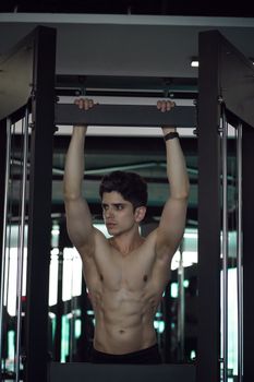 A young athletic man doing pull-ups in a modern indoor gym.