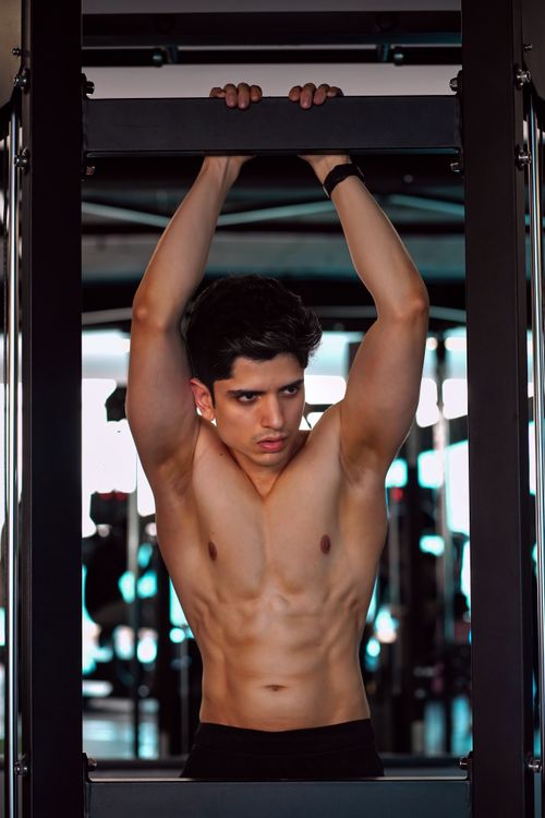 Free Muscular young man performing pull-ups on a bar in a modern gym setting. Stock Photo