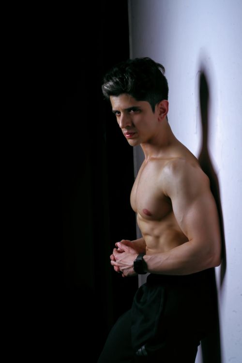 Free Athletic young man showing muscles in a dimly lit studio setting. Perfect for fitness and health-related projects. Stock Photo