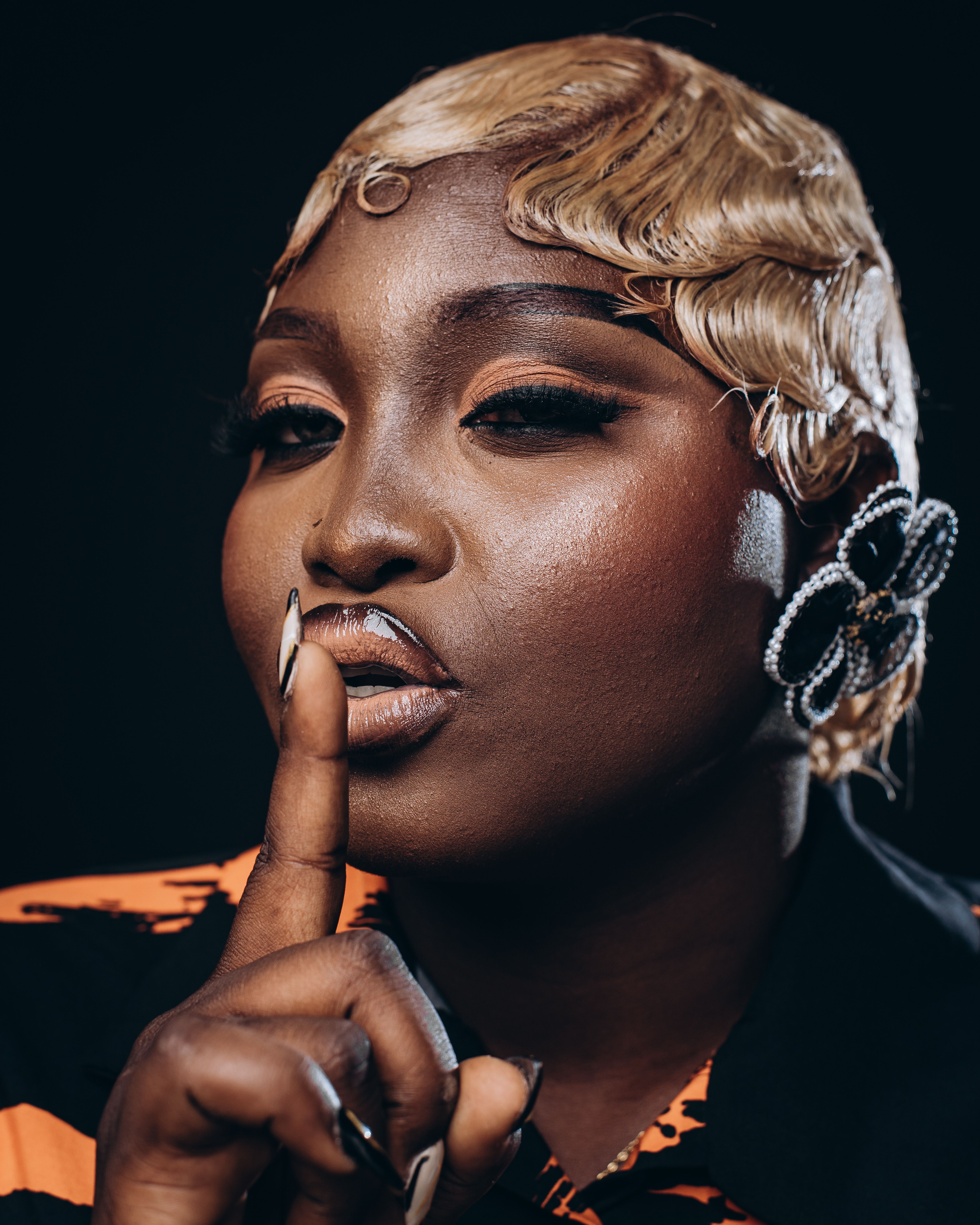 Glamorous portrait of a woman with styled hair, shushing gesture and bold accessories.