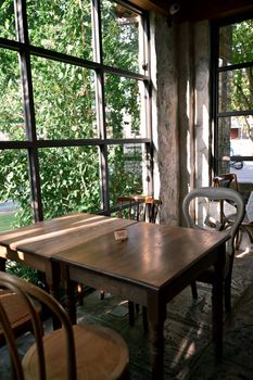 Wooden tables and chairs in a bright, sunlit cafe corner with a large window view.