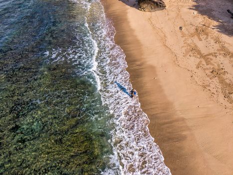Aerial shot of a tranquil beach in Bali, Indonesia with waves gently lapping the shore.