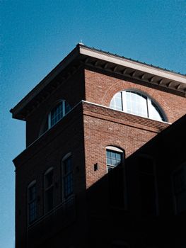 A stunning view of a historic brick building with arched windows and deep shadows contrasting the bright blue sky.