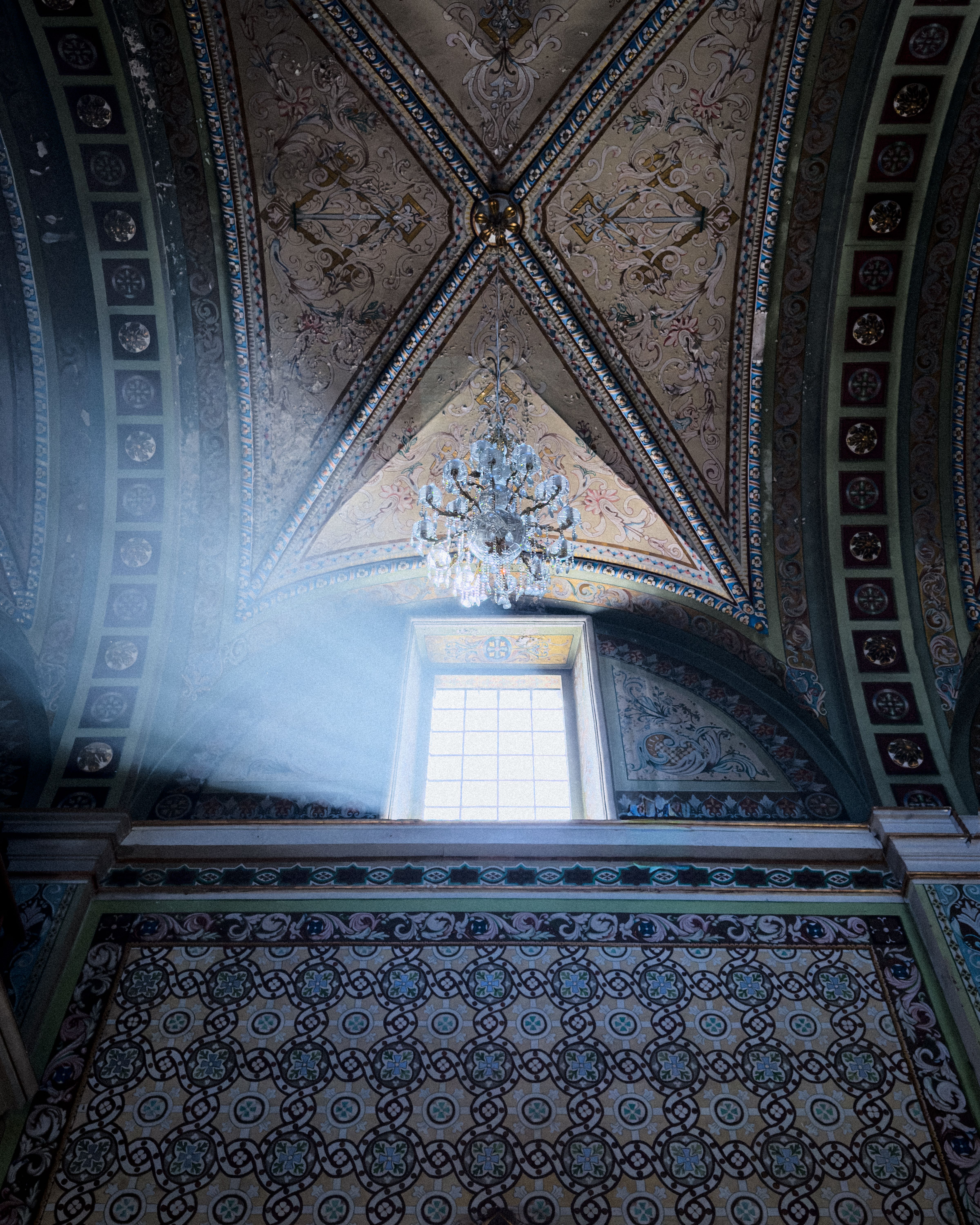 Captivating sunbeam through window highlights intricate mosaic and chandelier in historic Mexican architecture.