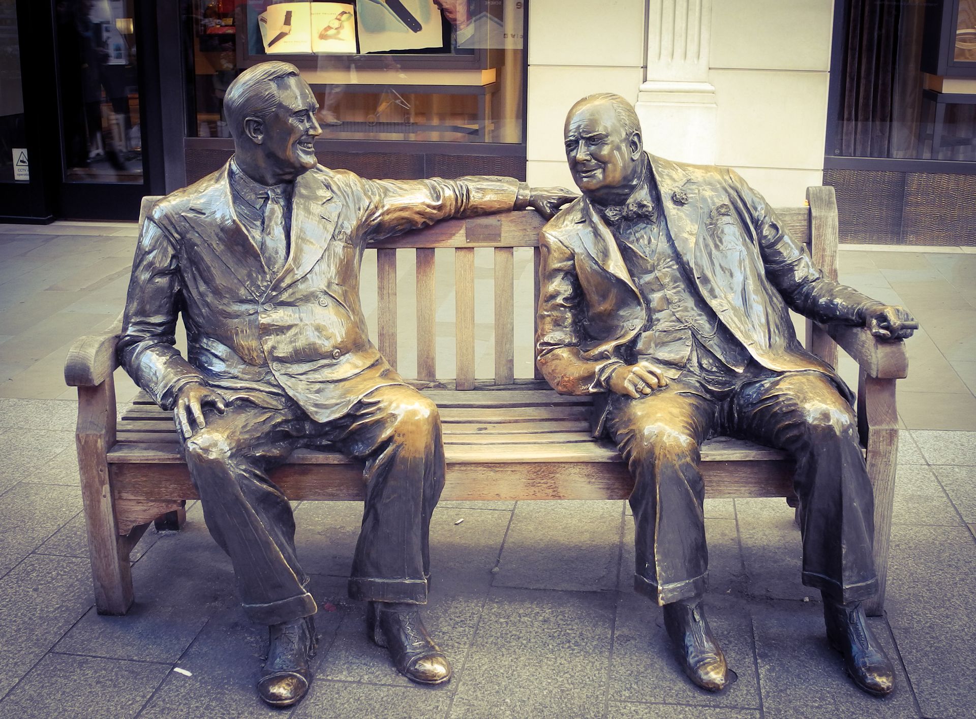 Bronze sculptures of two historic figures sitting on a bench, engaging in conversation.