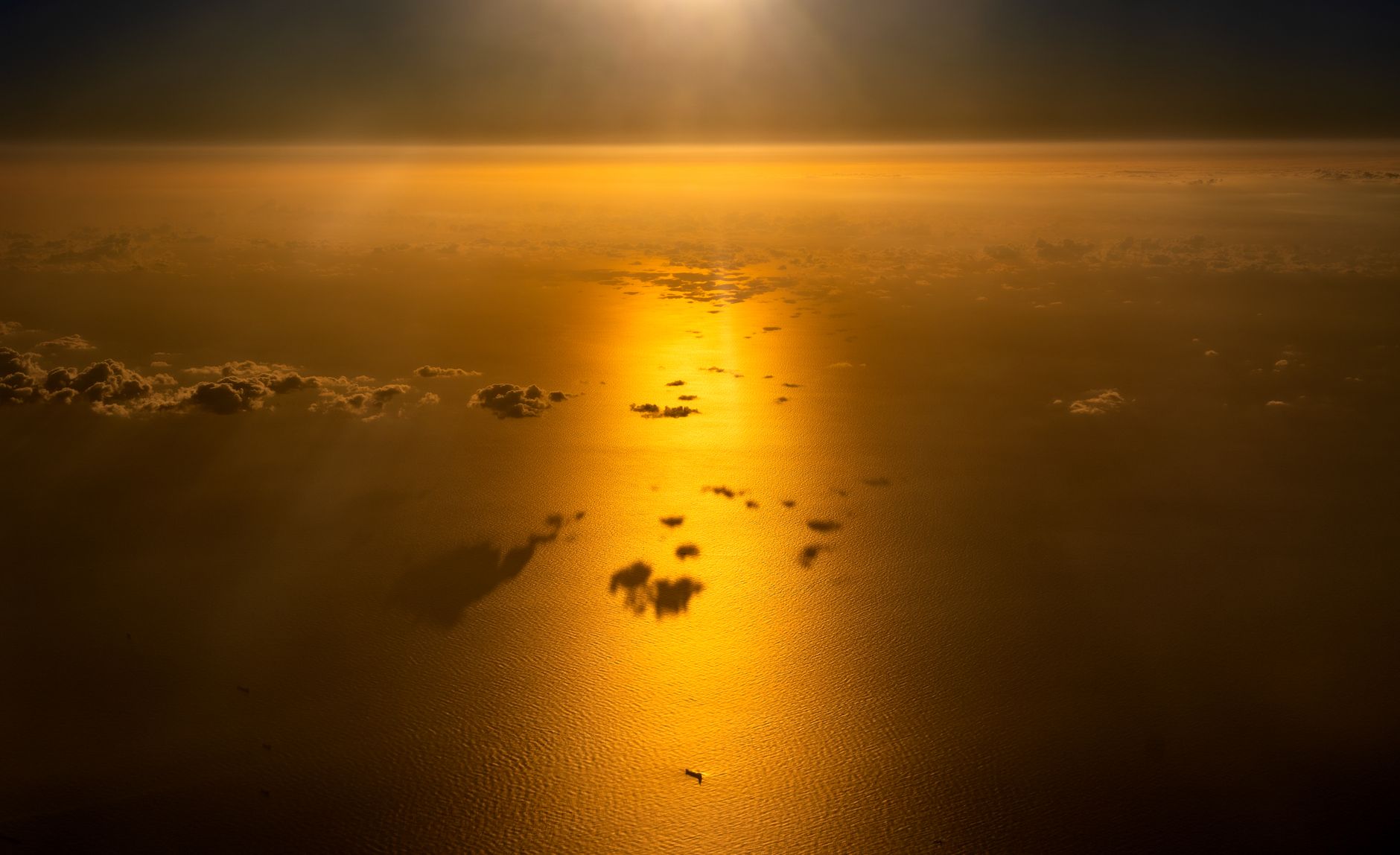 Golden sunrise reflecting over a peaceful ocean with scattered clouds and a distant ship.