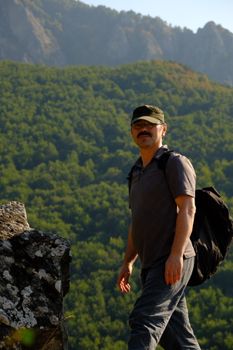 Adult man hiking in lush green mountain landscape on a sunny day.