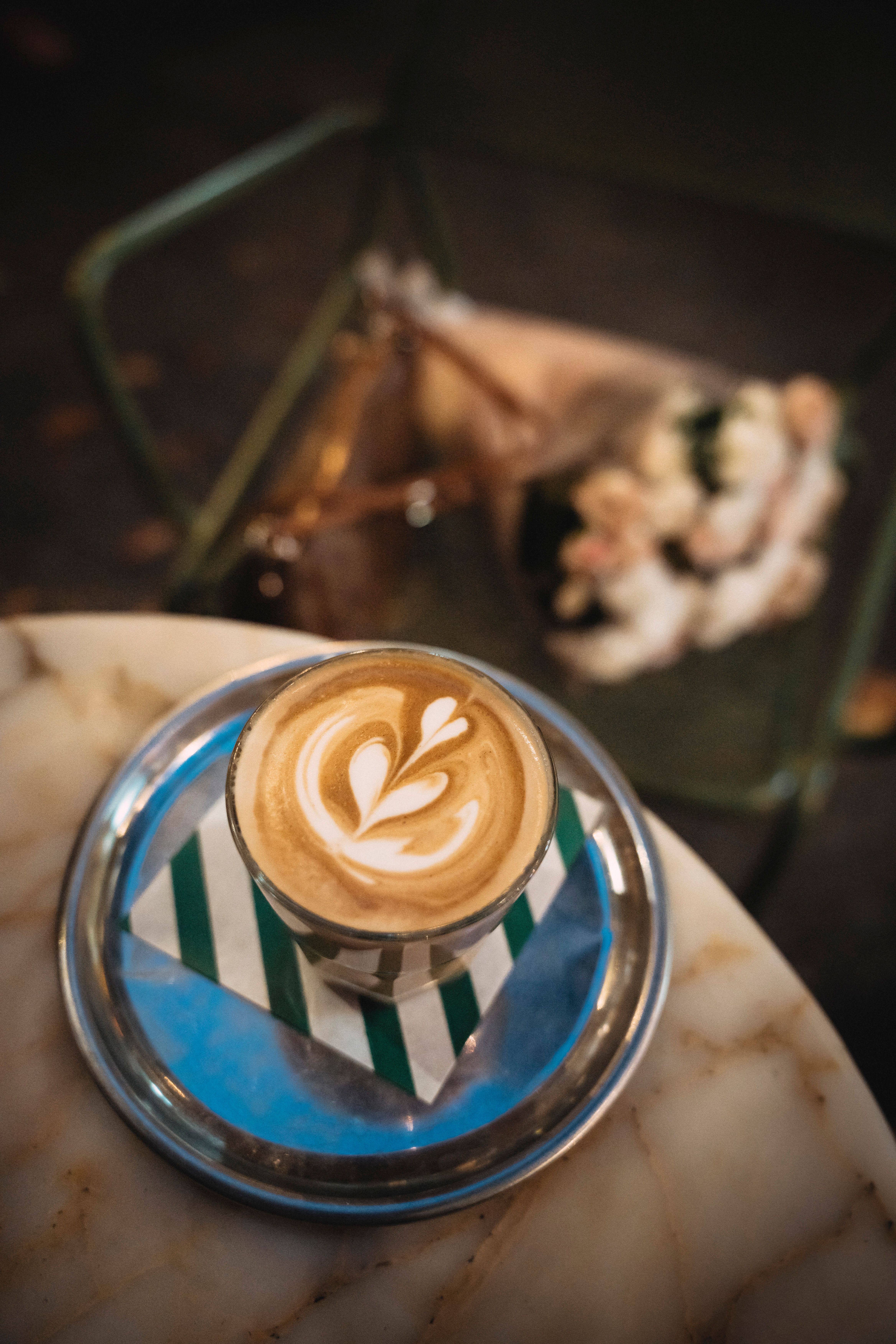 Beautifully crafted cafe latte with latte art on a marble table, set with a blurred floral arrangement in the background.