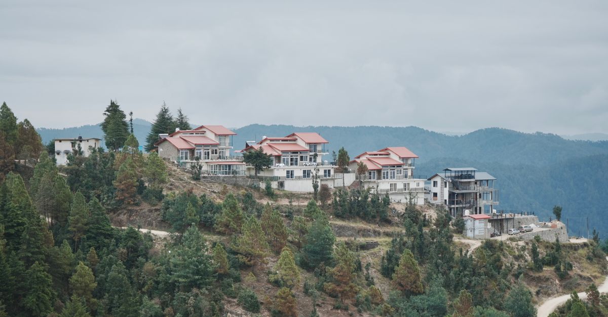 Aerial view of houses on a mountain ridge surrounded by pine trees on a cloudy day.