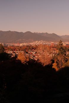 Stunning view of Vancouver cityscape with autumn foliage and warm sunset tones.