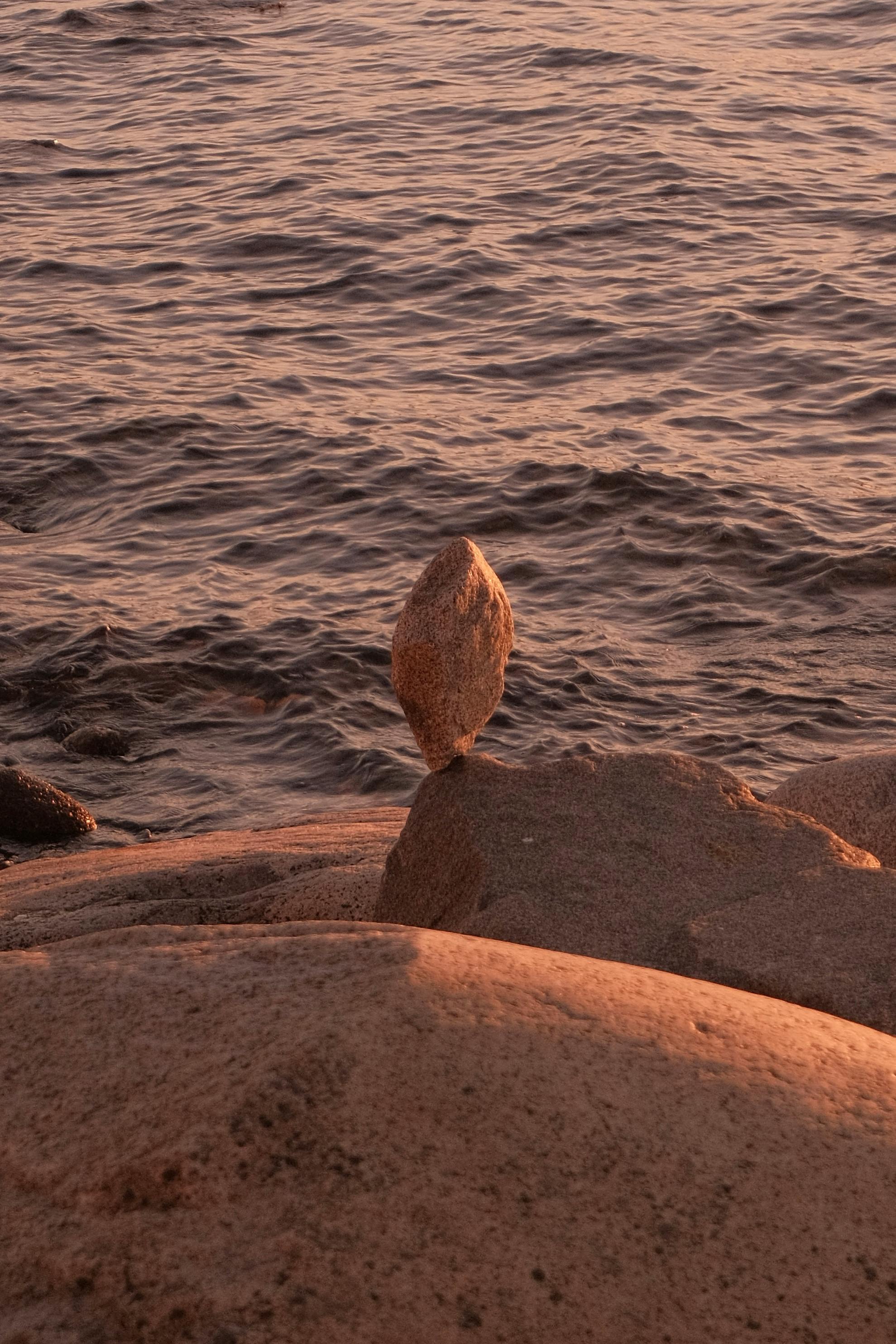 A tranquil coastal scene at sunset featuring a carefully balanced stone on the shore.