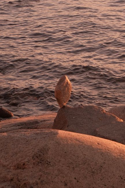 A tranquil coastal scene at sunset featuring a carefully balanced stone on the shore.