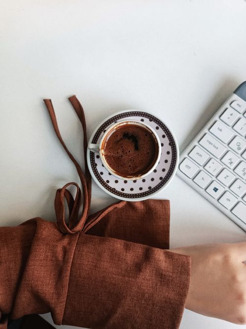 Free A person's arm rests beside a coffee cup and keyboard on a desk. Stock Photo