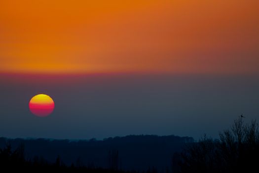 A colorful sunset with dramatic hues over a silhouetted landscape, creating a serene and vivid scene.
