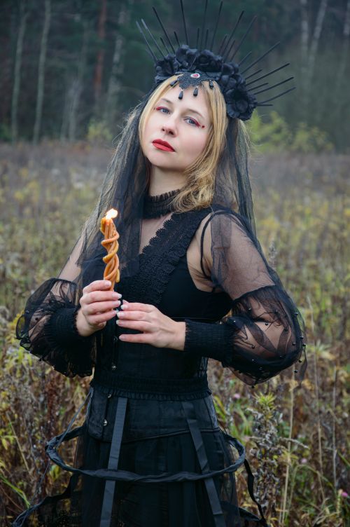 Free A woman in gothic clothing holds a candle in a field, creating a dramatic atmosphere. Stock Photo