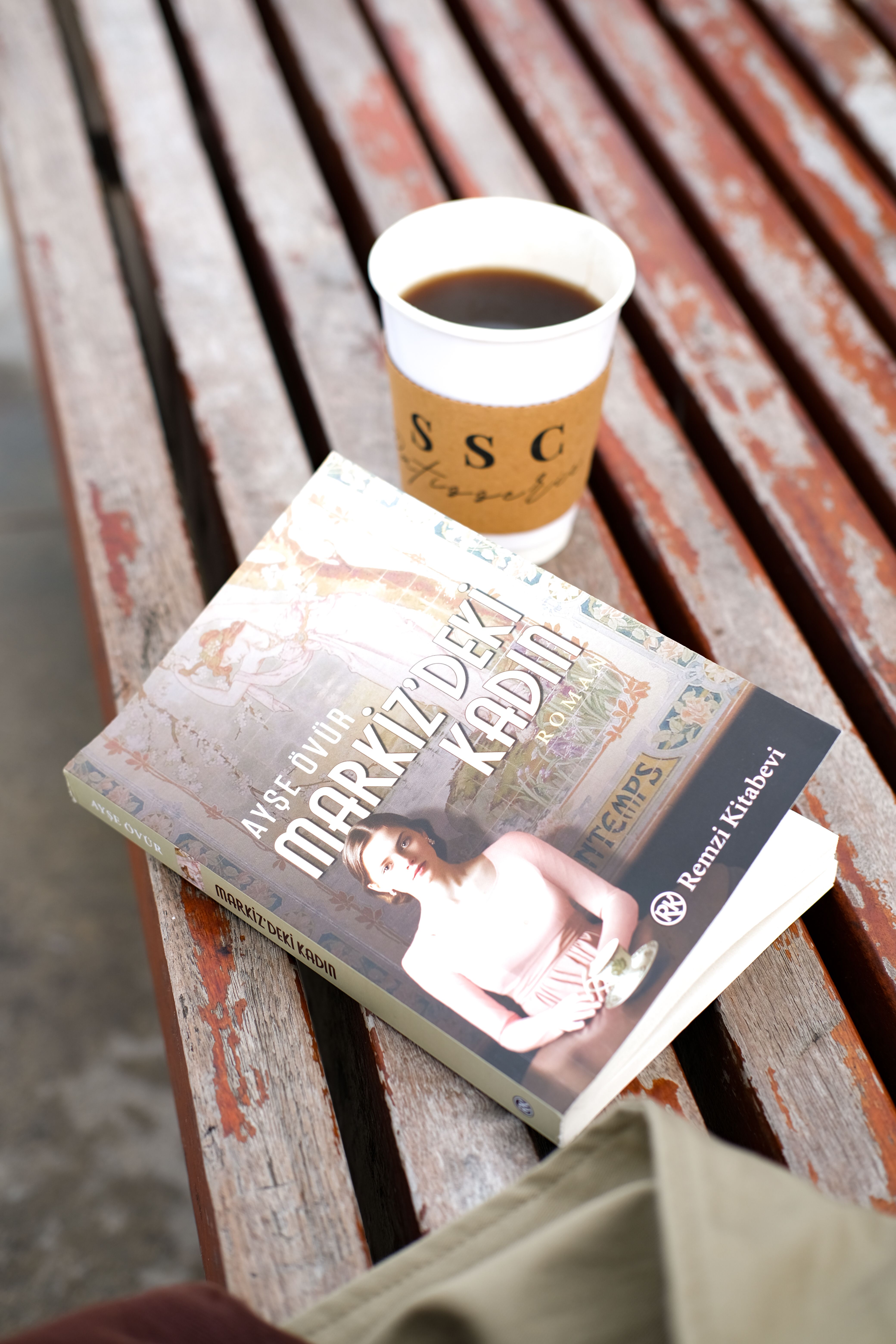 A cozy setup with a book and coffee on a park bench, ideal for relaxation.