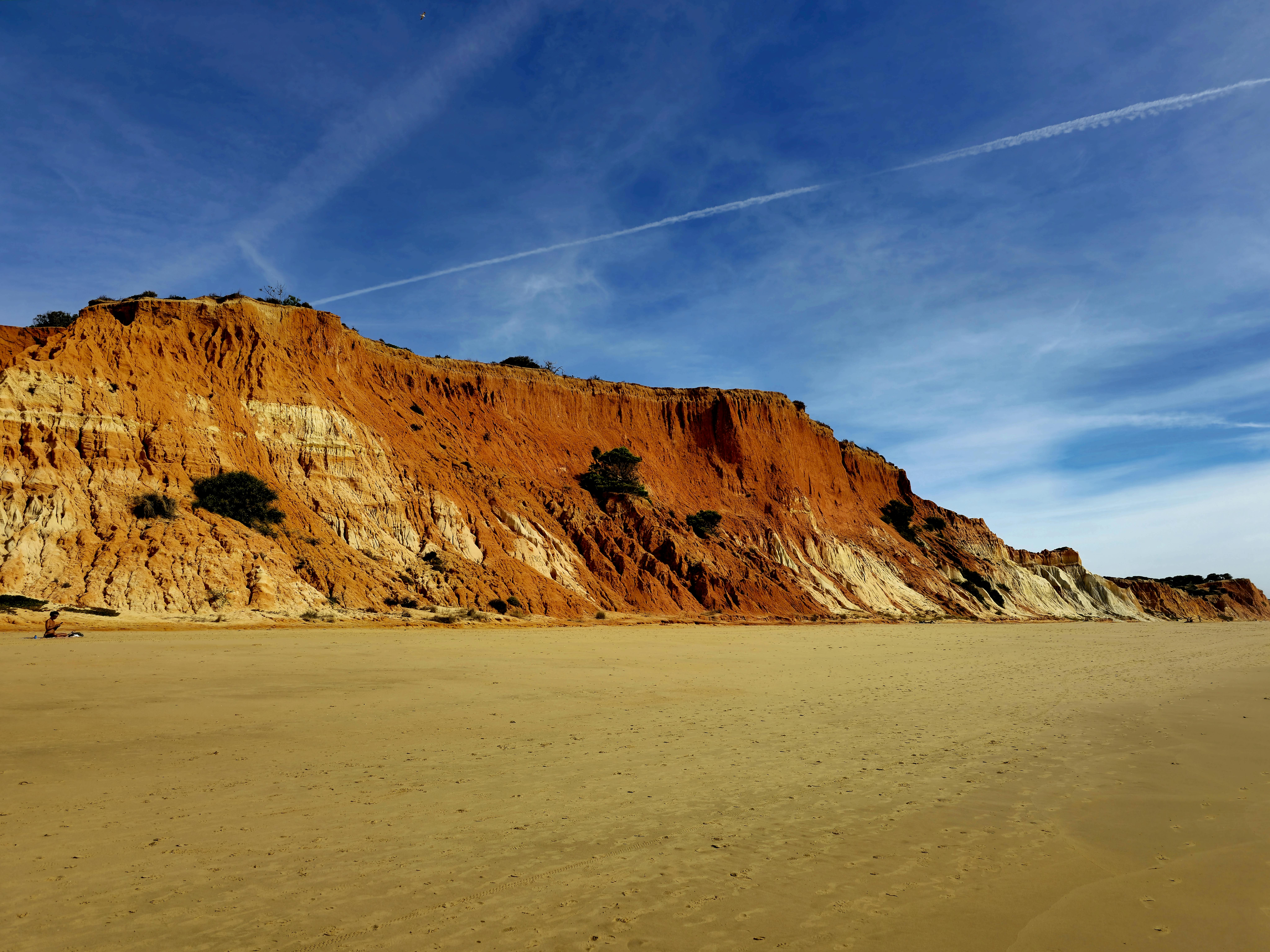 Breathtaking view of Praia da Falésia's red cliffs against a vibrant blue sky in Faro, Portugal.