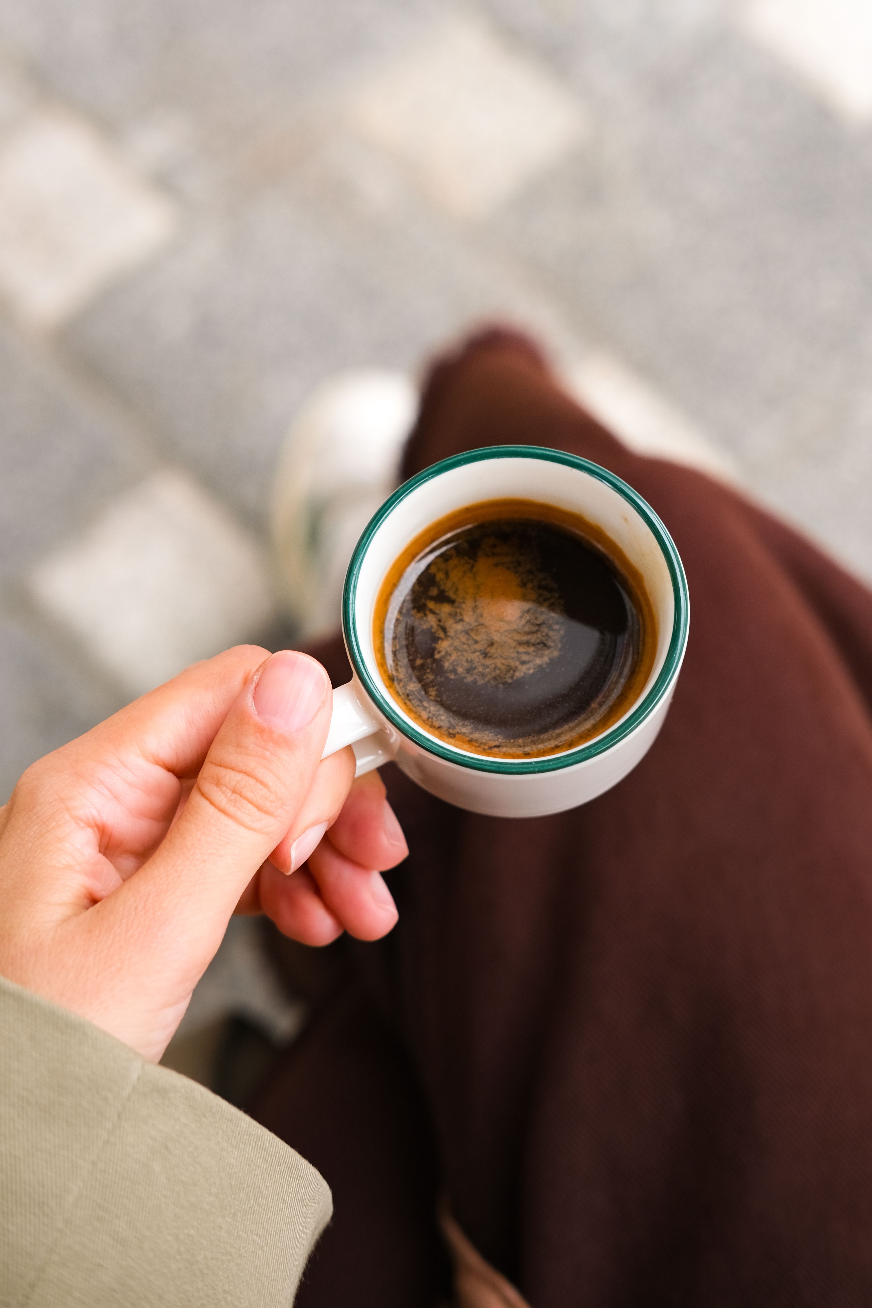 A person holds a small cup of espresso on a textured outdoor surface, creating a cozy moment.