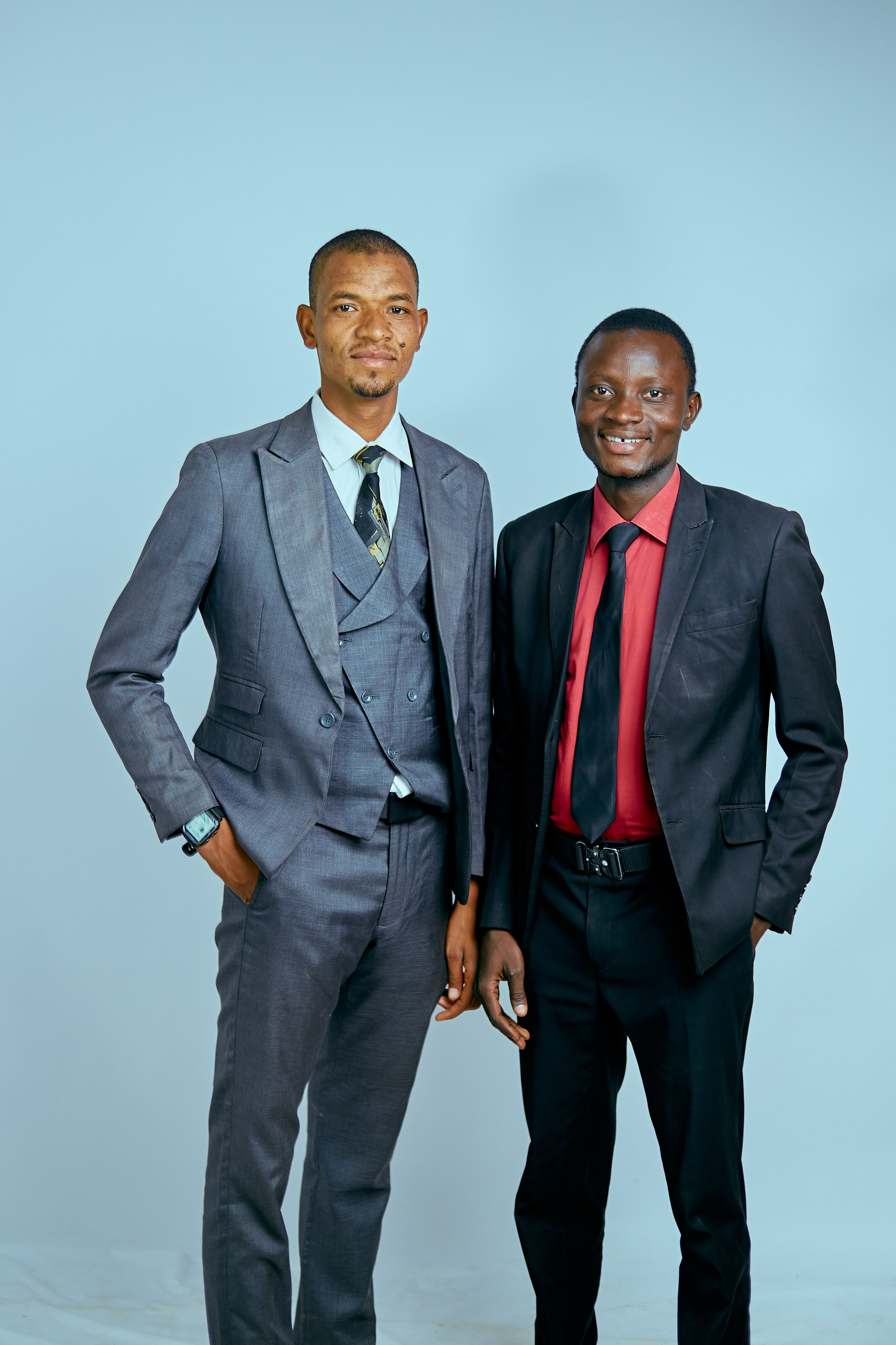 Two confident businessmen posing in formal attire against a neutral background.