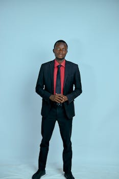 Professional portrait of an adult man in a black suit with a red tie on a blue background.